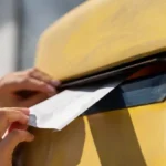 A close-up of hands placing a letter into a vintage mailbox, symbolizing a career growth mindset and the act of sending wisdom to one's younger self.