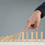 a hand stopping falling dominoes representing professional crisis management